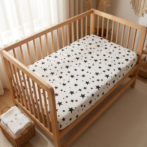 Berceau en bois habillé d'un drap housse bébé motif étoiles dans une chambre lumineuse