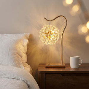 Lampe de table en cristal doré allumée sur une table de chevet dans une chambre élégante