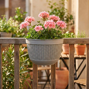 Pot mural gris en rotin tressé sur balustrade de balcon avec géraniums roses