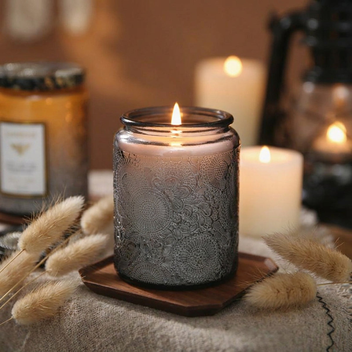 Bougie parfumée en pot en verre gris allumée sur plateau bois avec herbes séchées et éclairage ambiant