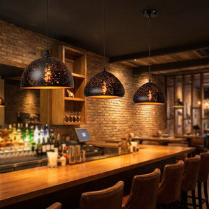 Trois suspensions vintage en fer noir dans un bar industriel, effet étoilé projeté sur les murs