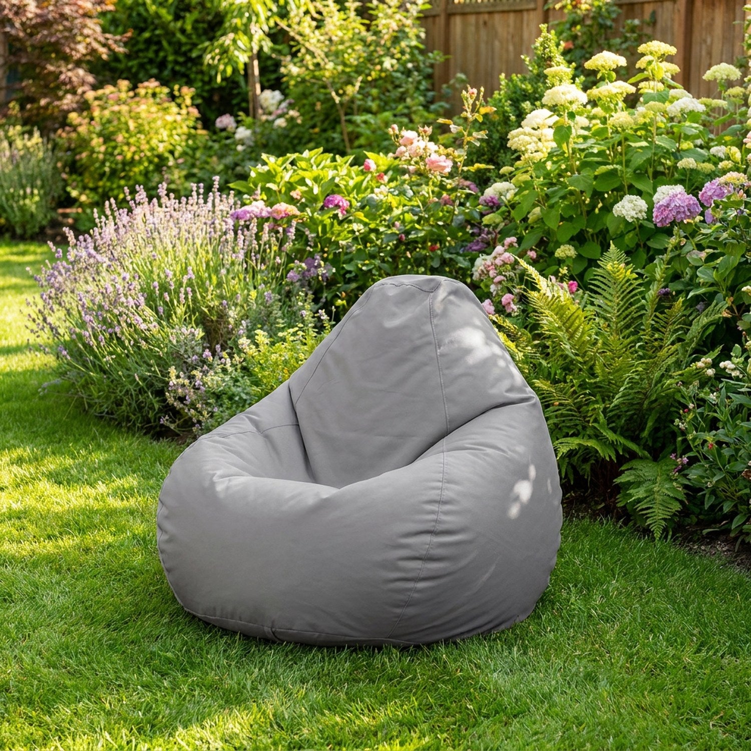 Housse de pouf poire grise installée sur une pelouse au milieu de fleurs de jardin