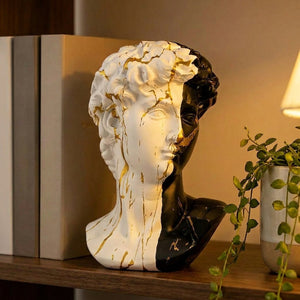Buste du David bicolore posé sur une étagère en bois entre des livres et une plante