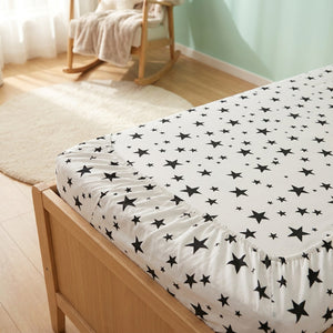 Drap housse bébé motif étoiles avec élastique visible près d'un fauteuil à bascule