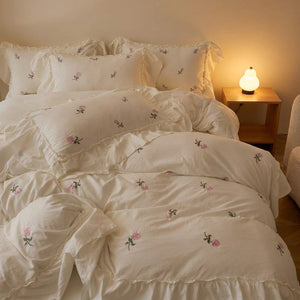 Parure de lit brodée de roses dans une chambre romantique avec table de chevet éclairée