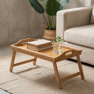 Plateau bambou pliant sur tapis en lin près d'un canapé beige avec livres et plante verte
