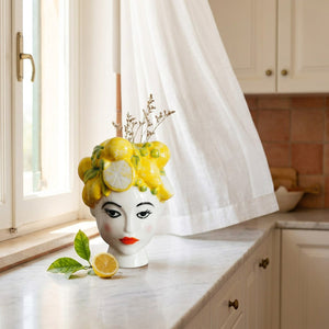 Vase portrait féminin en porcelaine blanche avec citrons jaunes posé sur un plan de travail en marbre près d'une fenêtre