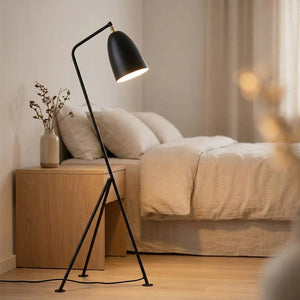 Lampadaire trépied noir à côté d'un lit dans une chambre cosy avec un vase