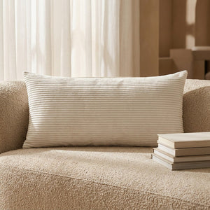 Traversin blanc en velours côtelé posé sur un canapé bouclette beige près de livres