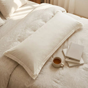Taie de traversin beige vue de dessus sur un lit avec tasse de thé et livres