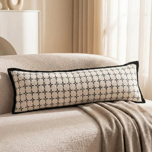 Traversin à motif quadrillé noir posé sur l'accoudoir d'un canapé bouclette avec un plaid taupe
