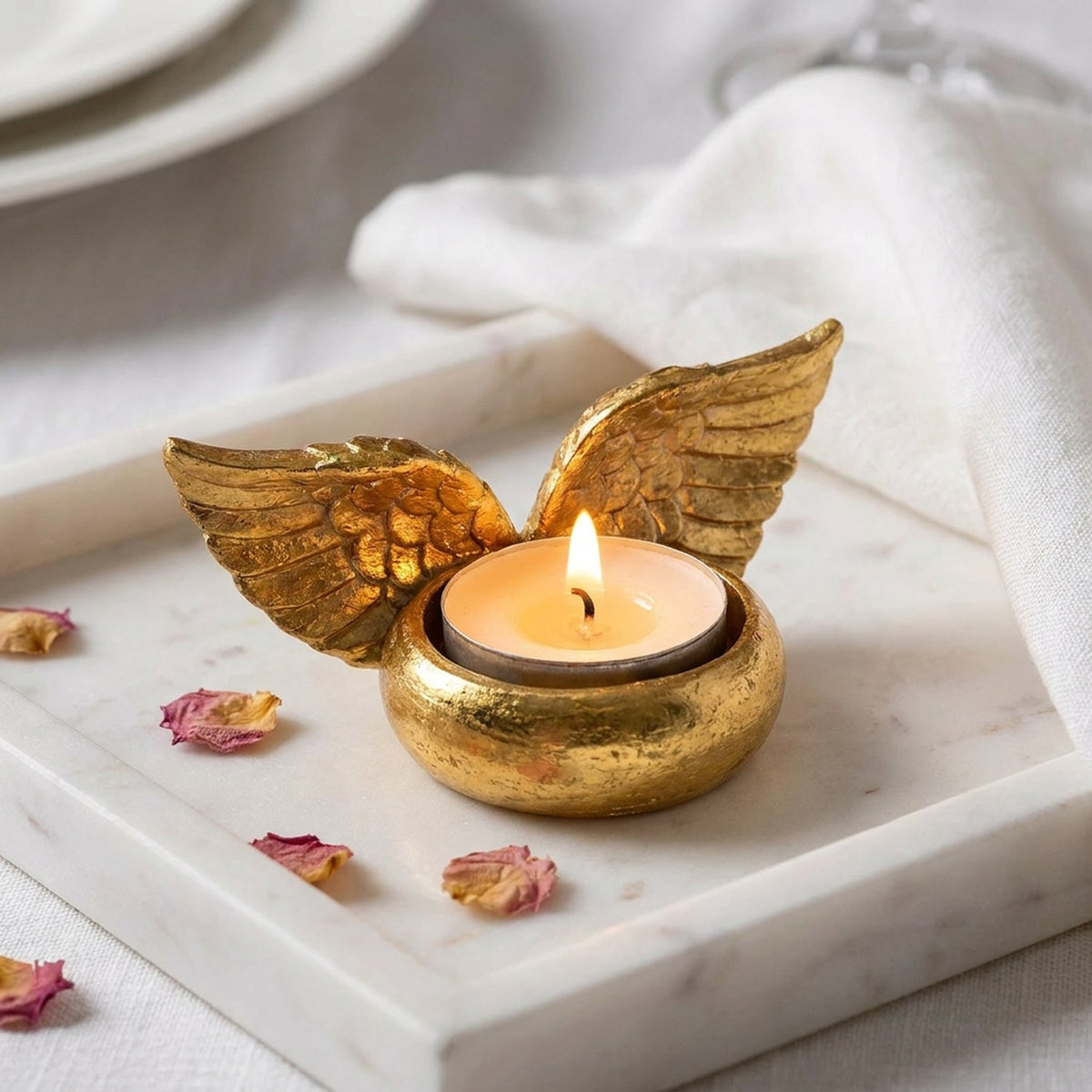 Bougeoir ailes d'ange doré avec bougie sur plateau marbre blanc et pétales de roses