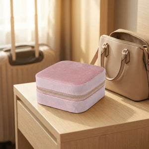 Boîte à bijoux de voyage en velours rose posée sur une table de nuit à côté d'un sac à main