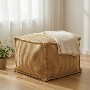 Pouf gaufré kaki posé dans un coin de chambre près d'une fenêtre