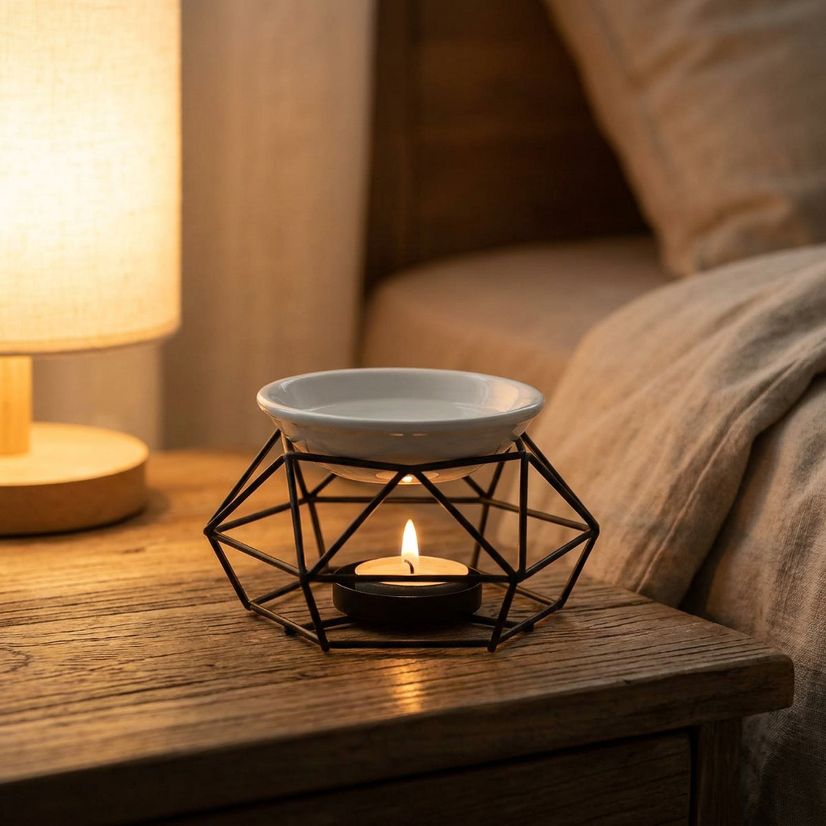 Brûle-parfum à bougie support métal noir posé sur une table de chevet dans une chambre chaleureuse