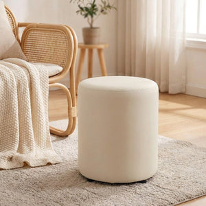 Tabouret pouf rond crème près d'un fauteuil en rotin avec un plaid tricoté