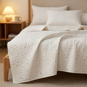 Couvre-lit blanc matelassé brodé d'étoiles sur un lit avec lampe de chevet chaleureuse