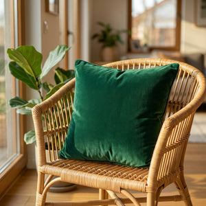 Coussin en velours vert émeraude posé sur un fauteuil en rotin près d'une fenêtre