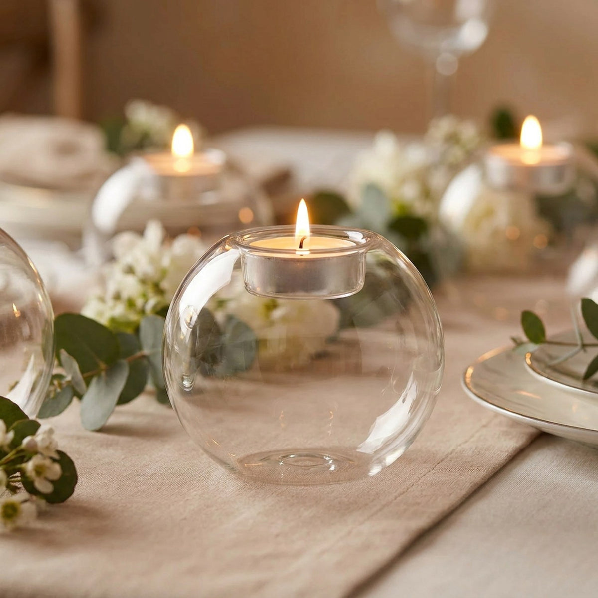Bougeoir boule en verre allumé sur une table de mariage avec eucalyptus et fleurs blanches