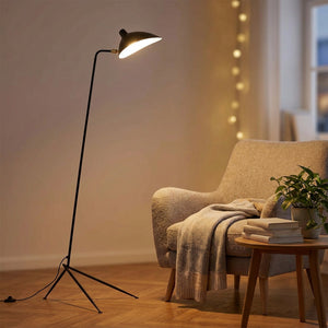 Lampadaire trépied une tête en métal noir allumé près d'un fauteuil cosy