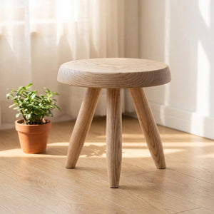 Tabouret rond en bois clair servant de support pour une plante près d'une fenêtre
