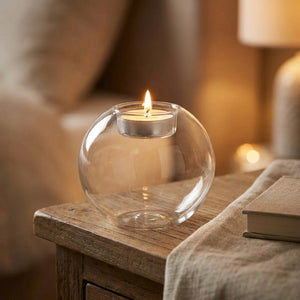 Bougeoir boule en verre allumé sur une table de chevet en bois dans une ambiance cosy