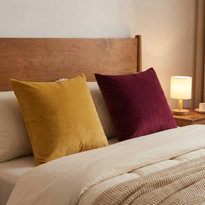 Coussins en velours moutarde et bordeaux sur un lit avec tête de lit en bois