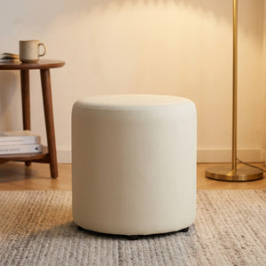 Tabouret pouf rond crème dans un coin lecture éclairé par un lampadaire