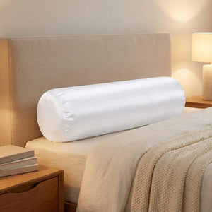 Traversin cylindrique satiné blanc appuyé contre une tête de lit dans une chambre chaleureuse