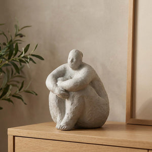 Statue de femme ronde grise assise repliée sur une console en bois