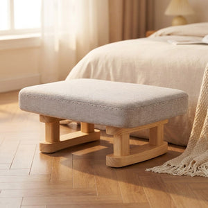Tabouret rembourré gris en bois posé au pied d'un lit dans une chambre chaleureuse