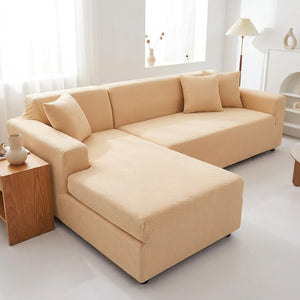 Housse de canapé extensible beige installée sur un canapé d'angle moderne dans un salon lumineux