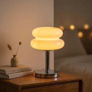 Lampe de chevet en verre forme macaron allumée diffusant une lumière chaude sur une table de nuit