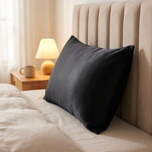 Taie d'oreiller satin noir posée sur un lit fait dans une chambre chaleureuse