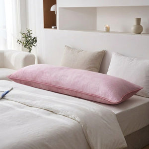Taie d'oreiller longue en velours rose posée sur un lit avec des coussins beiges