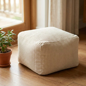 Tabouret pouf blanc en velours côtelé posé au sol près d'une fenêtre