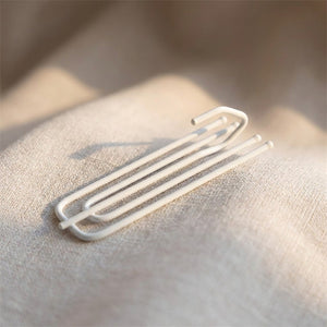 Crochet de rideau blanc à quatre broches métalliques posé sur un tissu en lin clair