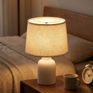 Abat-jour tambour en lin naturel beige posé sur une lampe de chevet en céramique allumée
