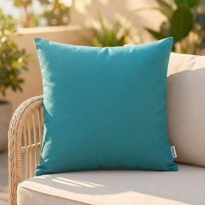Housse de coussin extérieur imperméable turquoise posée sur un canapé de jardin en rotin