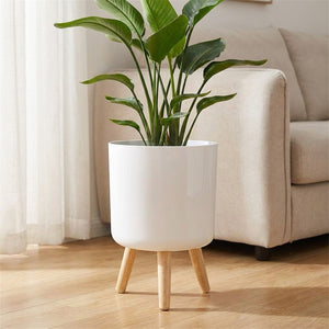 Cache-pot blanc sur pieds en bois avec une plante verte dans un salon scandinave lumineux