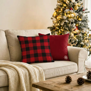Deux housses de coussin de Noël à carreaux rouges posées sur un canapé beige près d'un sapin décoré