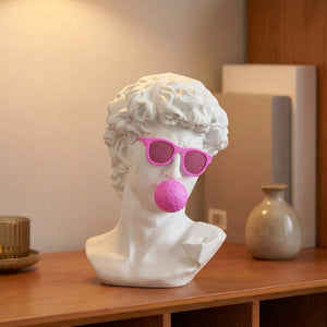 Buste de David en résine blanche avec lunettes roses WOW et bubblegum posé sur une étagère en bois