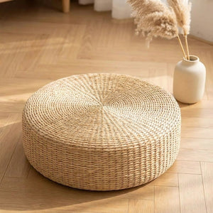 Pouf rond en paille tressée naturelle posé sur un parquet clair dans une ambiance zen