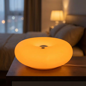 Lampe beignet Bauhaus allumée en orange sur une table de chevet