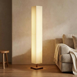 Lampadaire colonne en tissu plissé crème allumé sur base en bois dans un salon Japandi