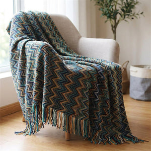 Plaid tricoté à motifs chevrons multicolores et franges drapé sur un canapé bleu