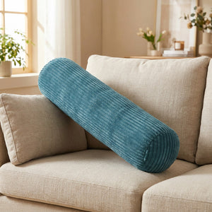 Traversin cylindrique en velours côtelé bleu foncé posé contre les coussins d'un canapé beige