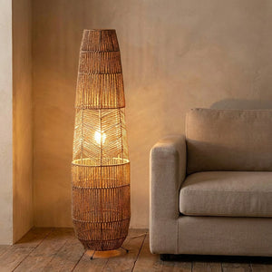 Lampadaire en rotin tressé allumé d'une lumière chaude posé dans un salon cosy près d'un canapé beige