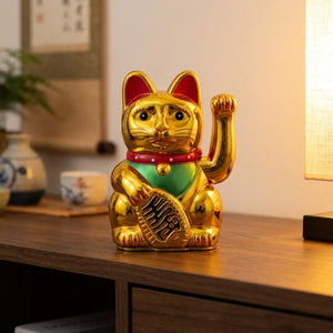 Figurine chat porte-bonheur doré à bras animé posée sur une console en bois dans un intérieur chaleureux