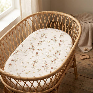 Deux draps-housses de berceau en gaze de coton à fleurs posés dans un couffin en osier d une chambre bébé